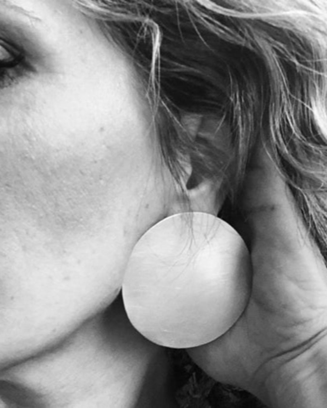 Close-up of a person wearing large round metallic earring.