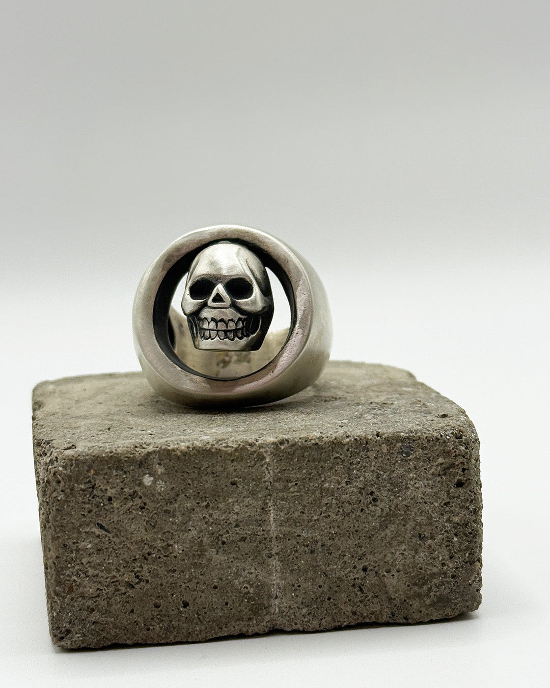 Silver skull ring on a concrete block with a white background