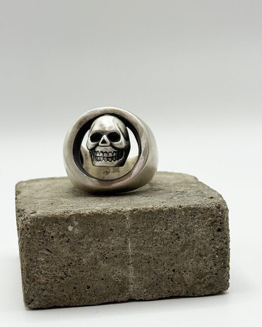 Silver skull ring on a concrete block with a white background