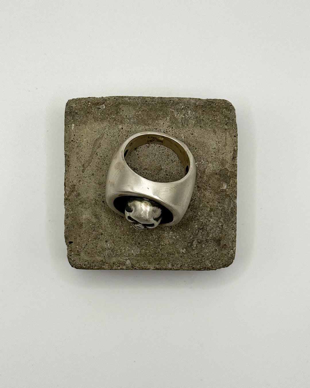 Silver ring on a square stone surface with a plain background