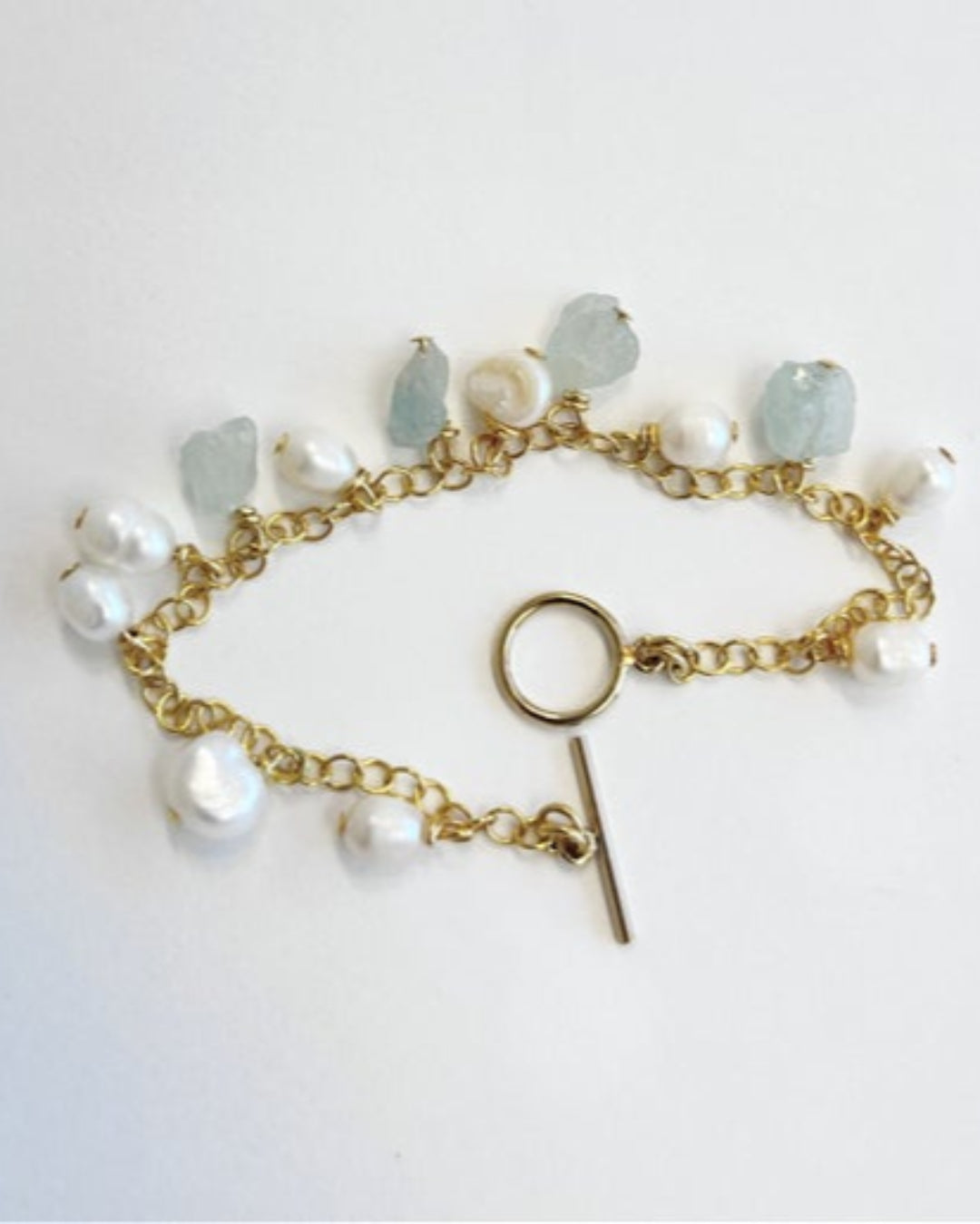 Gold bracelet with pearls and gemstones on a white background
