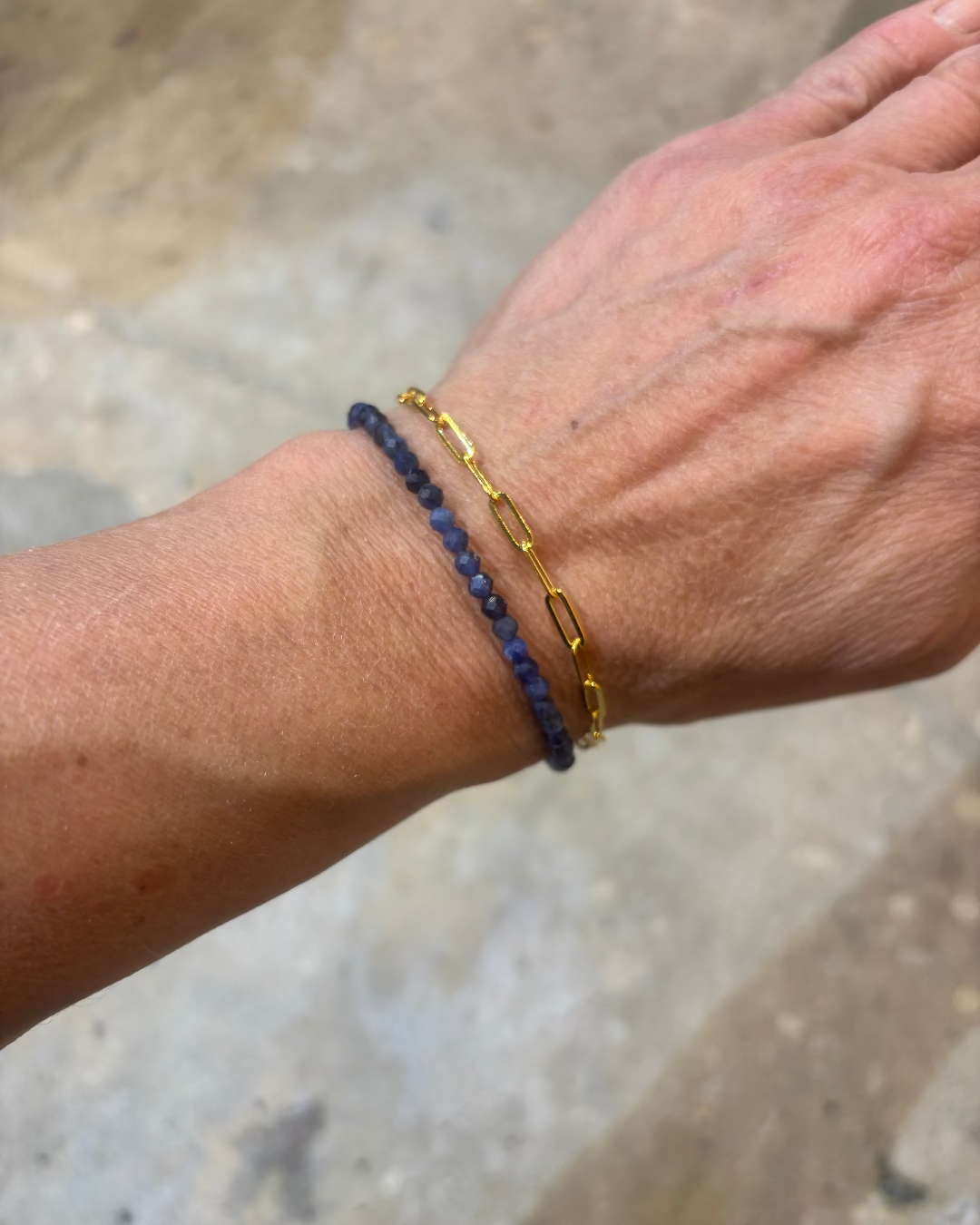 Two bracelets, one blue and one gold, on a wrist with a blurred background.