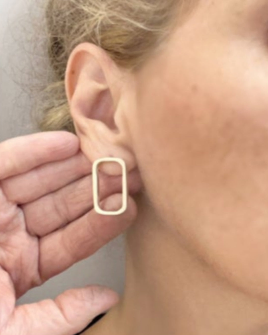 Gold square hoop earring worn by a person with a neutral background