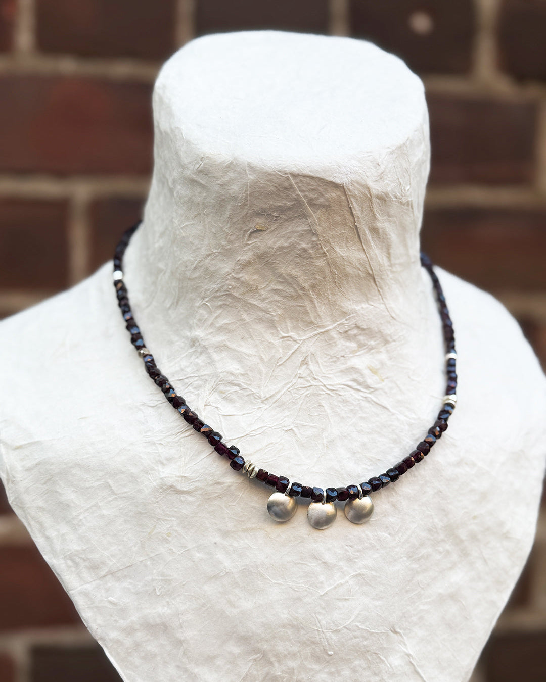 Necklace with beads on a mannequin bust against a brick wall background
