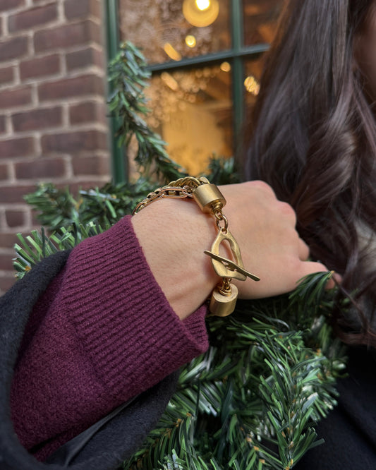 Person wearing a gold bracelet with a purple sleeve against a blurred festive background