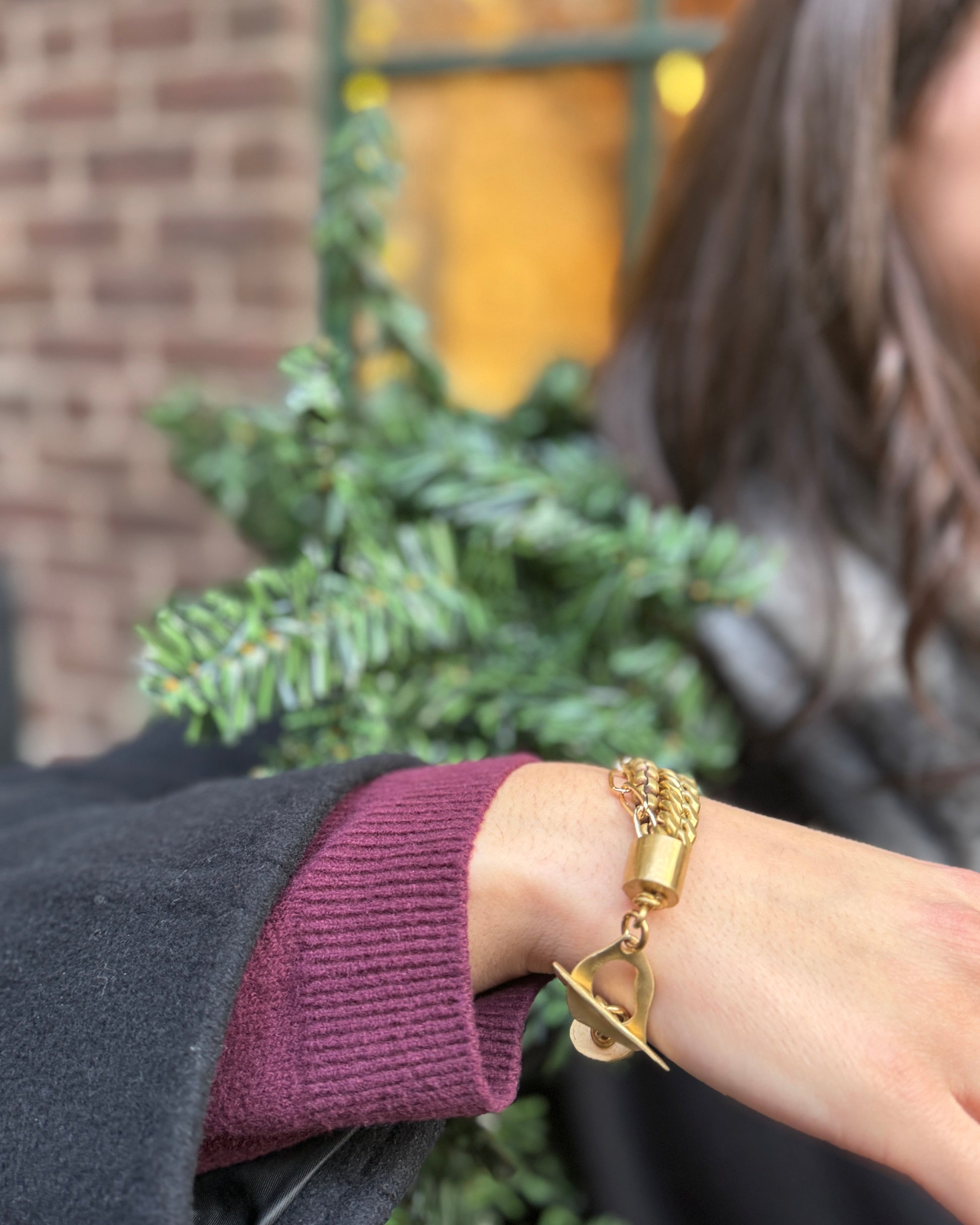 Close-up of a person's wrist wearing a gold bracelet with a blurred background