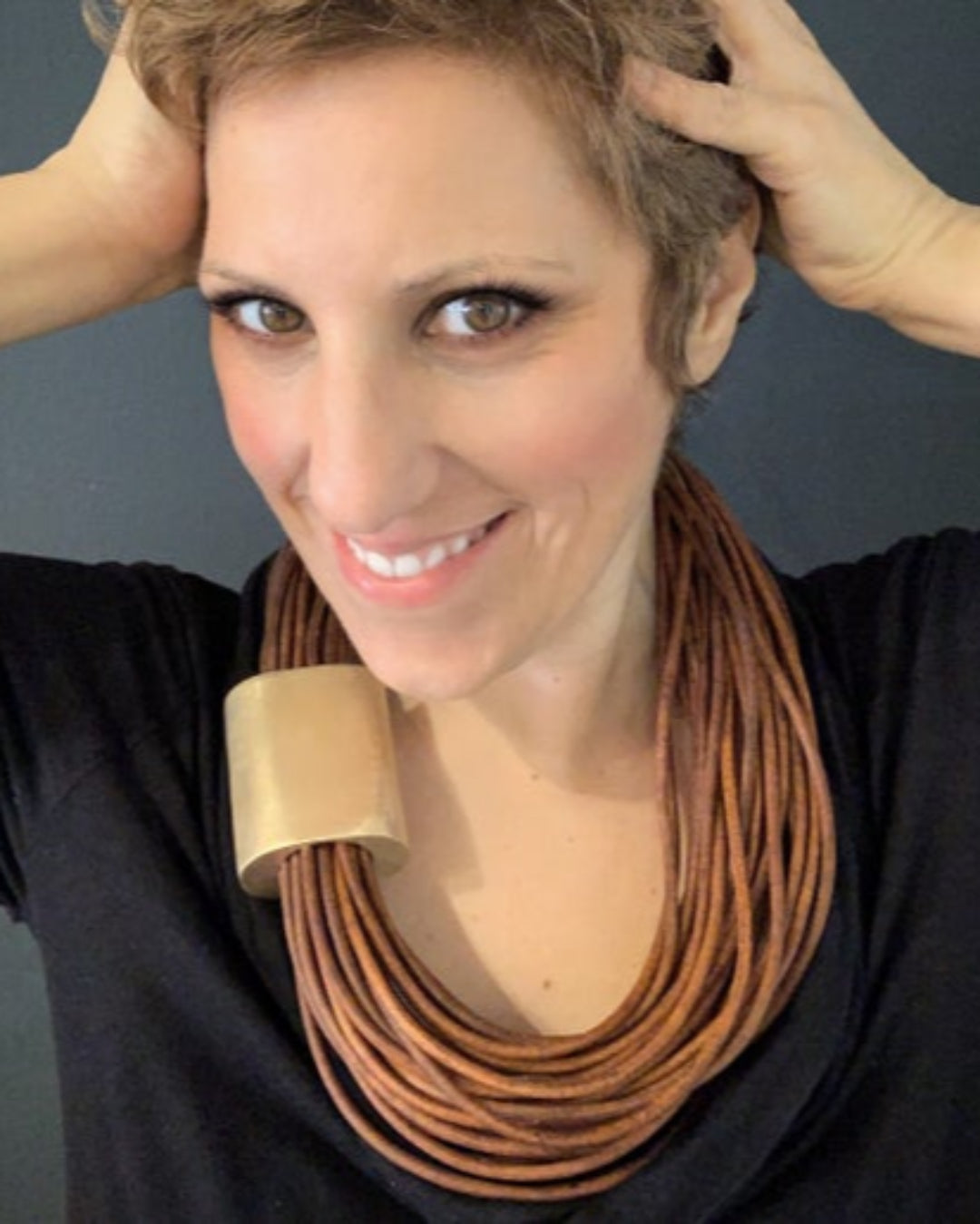 Woman wearing a multistrand brown leather necklace against a gray background