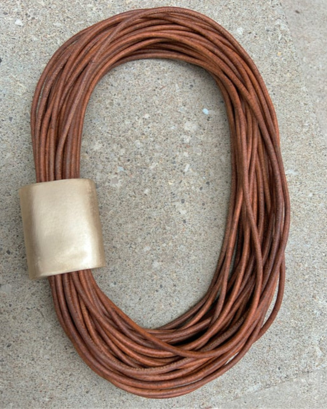 Multistrand leather necklace with bronze detail on a concrete surface