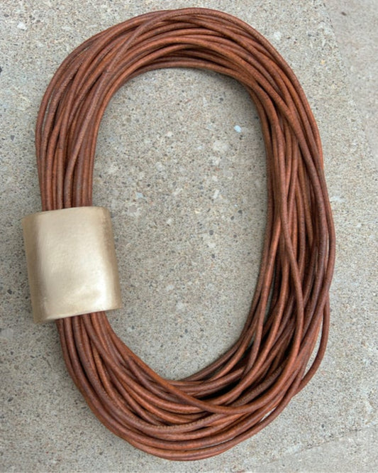 Multistrand leather necklace with bronze detail on a concrete surface