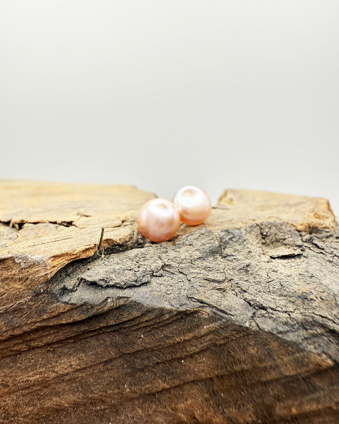 Two pink pearls on a piece of wood with a light gray background