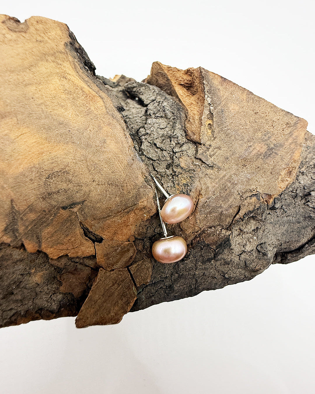Pair of pearl earrings on a piece of wood with a white background