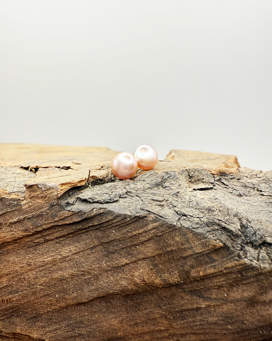 Pair of pink pearls on a wooden surface with a light gray background