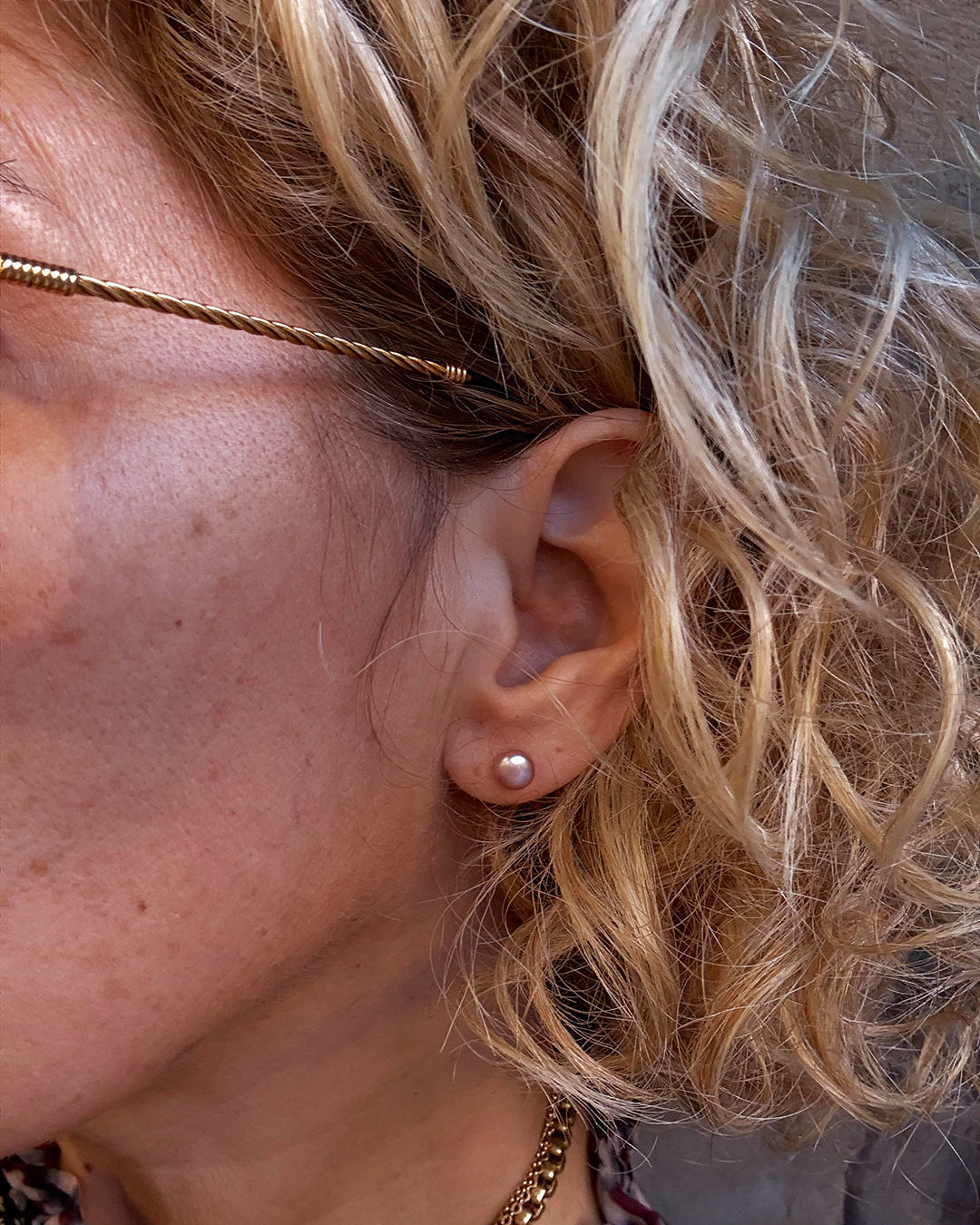 Close-up of a person wearing a gold earring and pearl stud earring.