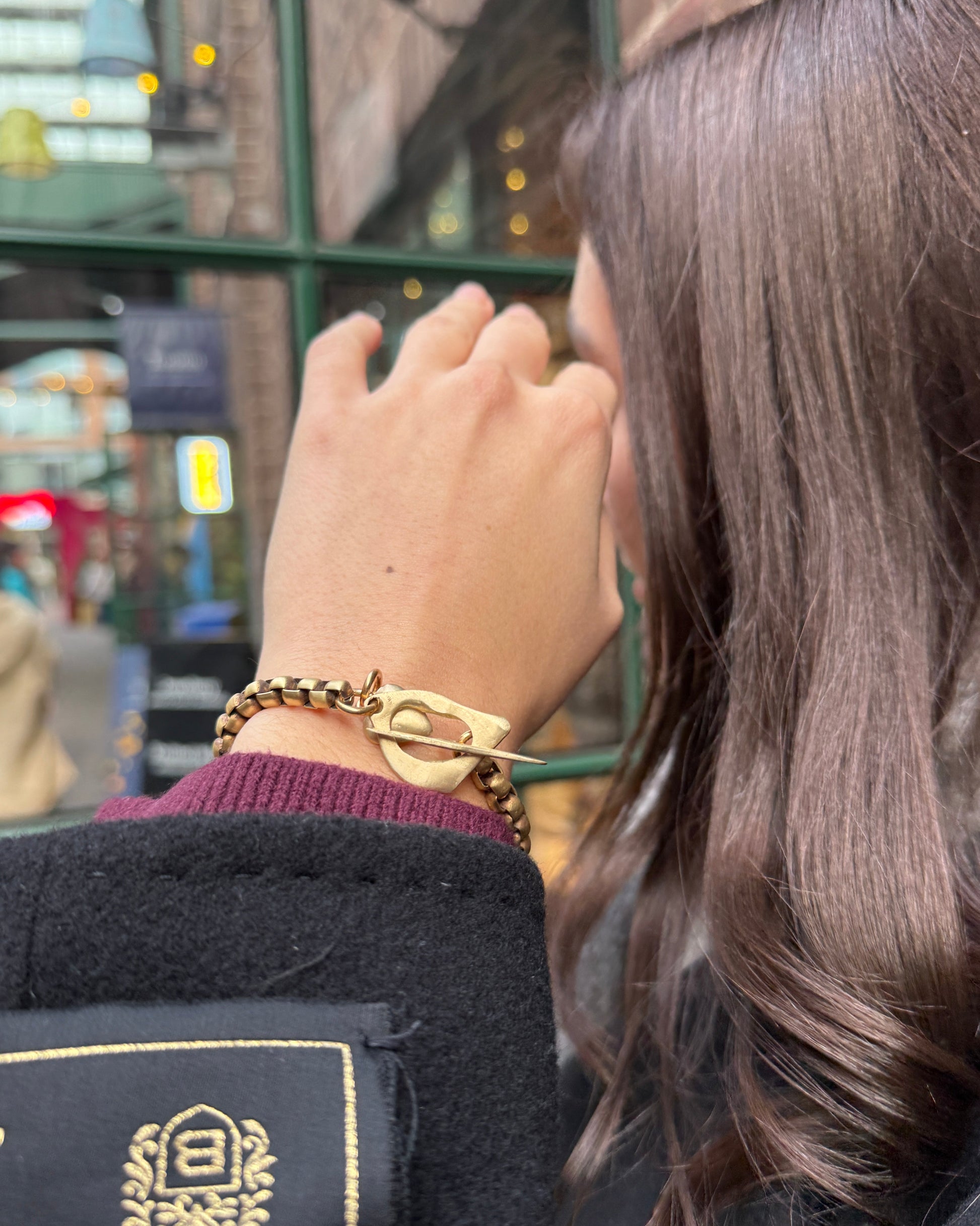 Person wearing a gold watch and bracelet with a blurred background