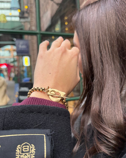 Person wearing a gold watch and bracelet with a blurred background