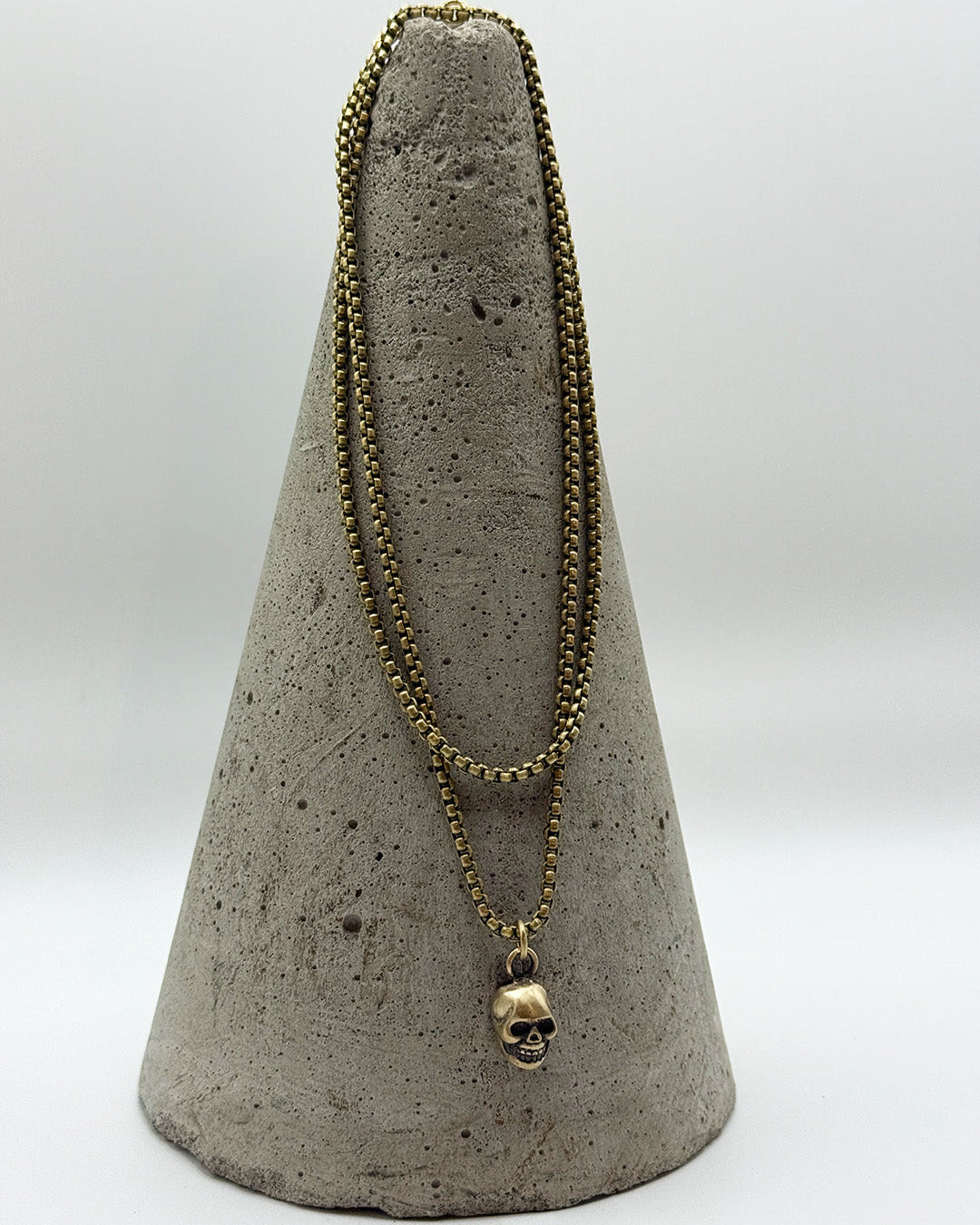 Gold necklace with a skull pendant on a gray cone stand against a white background