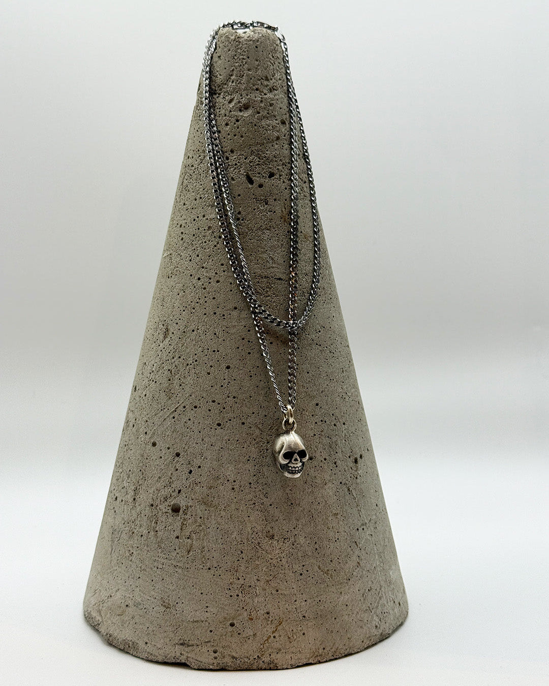 Necklace with a skull pendant on a concrete cone against a white background