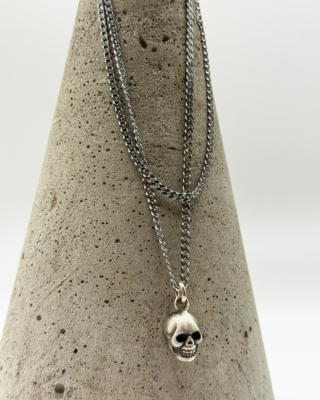 Silver skull pendant necklace on a concrete block with a white background