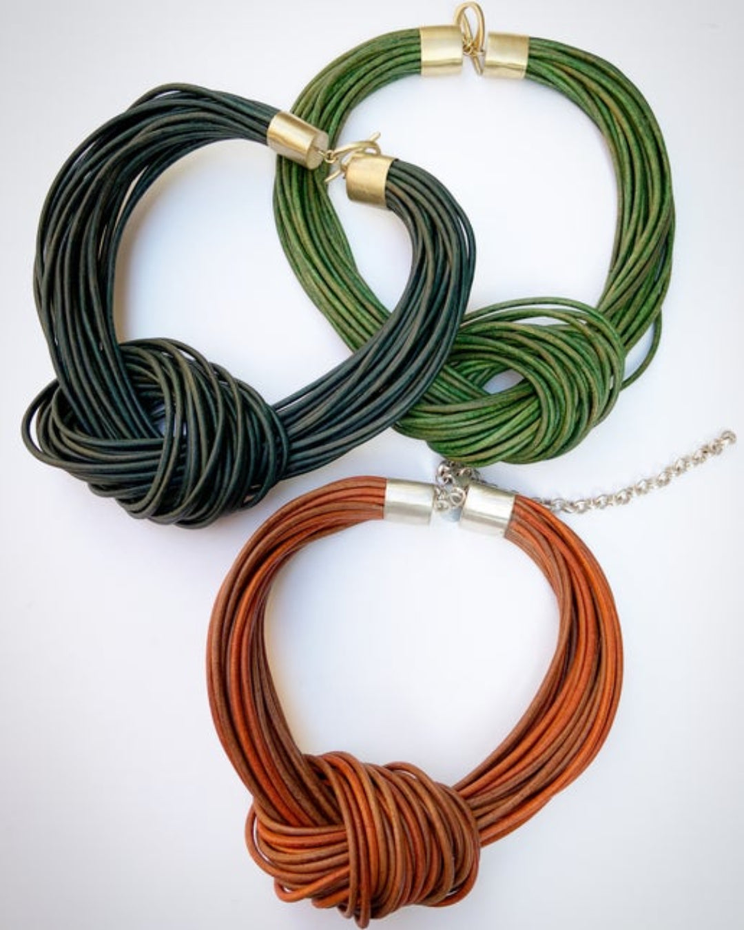 Three multistrand leather necklaces in green, brown, and gold on a white background