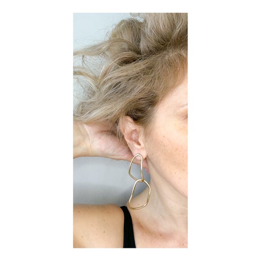 Gold  double hoop earring worn by a person with blonde hair on a neutral background