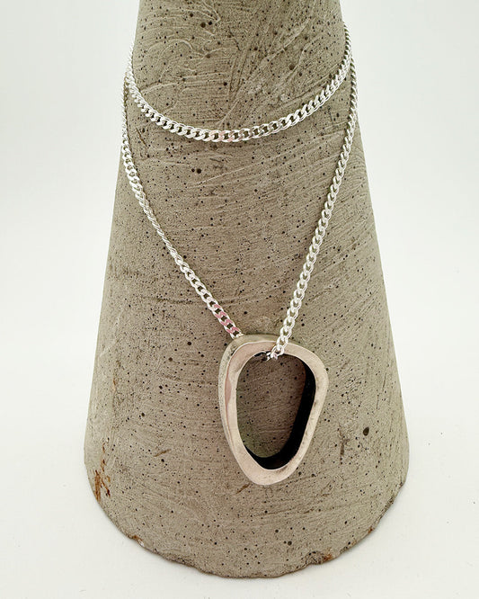 Silver necklace with a unique pendant on a textured stone stand against a white background