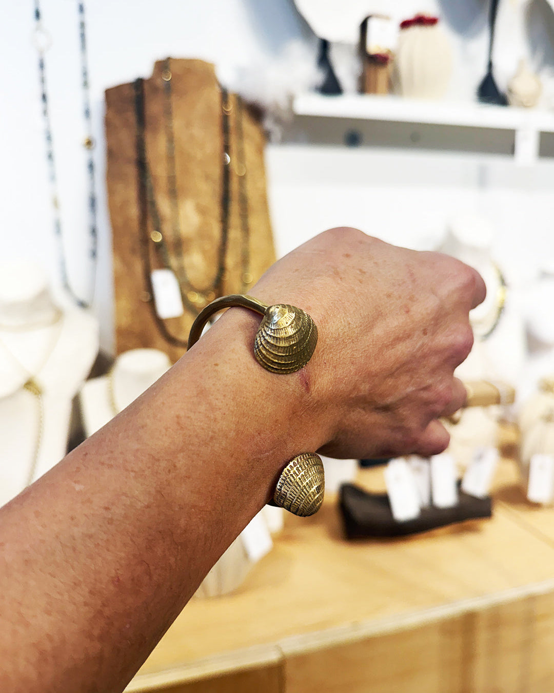 Hand wearing a gold bracelet with a blurred store background