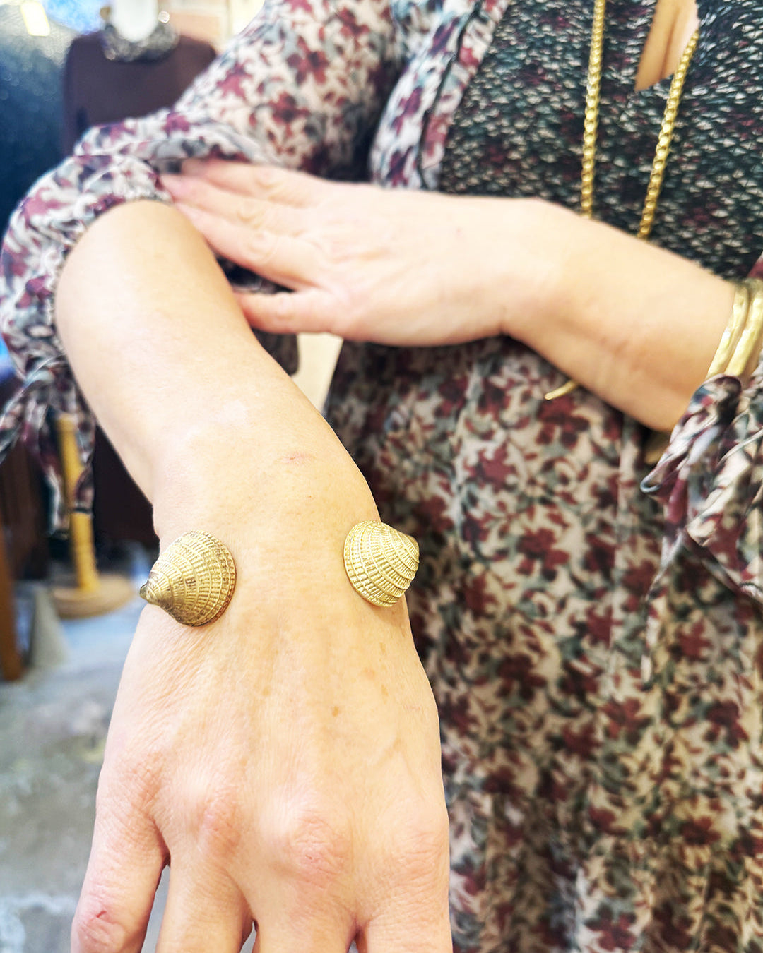 Close-up of a person's arm wearing a gold bracelet with shell design.