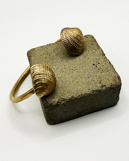 Gold shell-shaped earrings on a concrete block with a white background