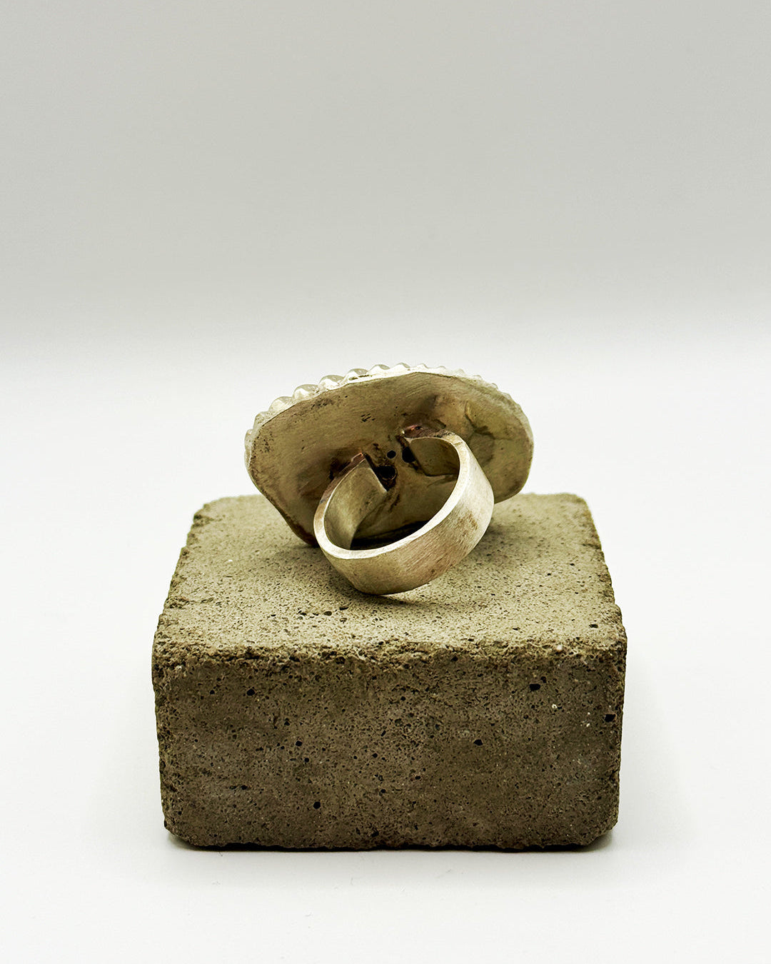 Silver ring on a textured stone block with a white background
