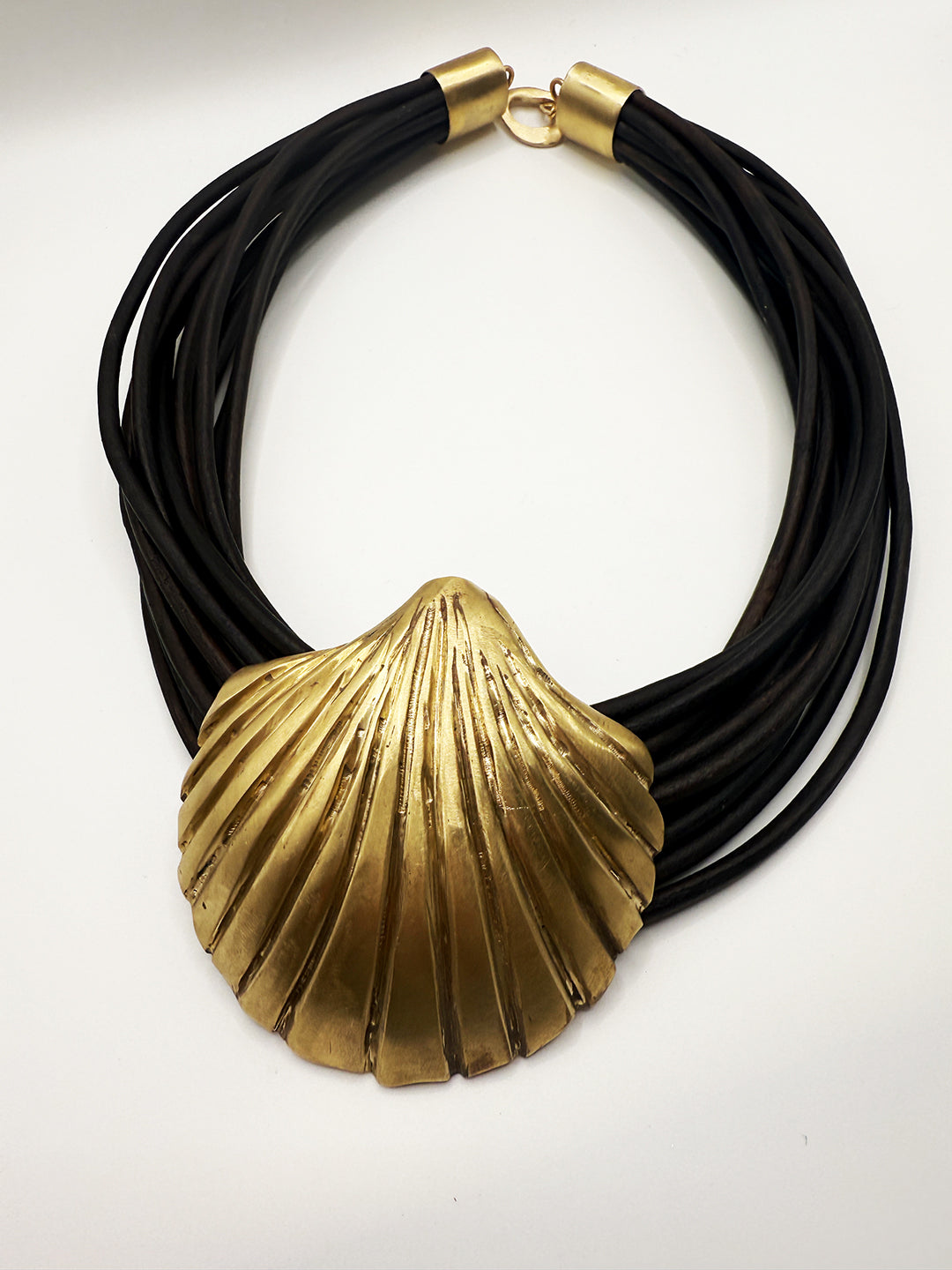 Necklace with black cord and gold shell pendant on a white background