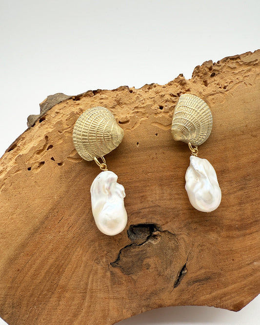 Pair of earrings with shell and pearl designs on a wooden surface