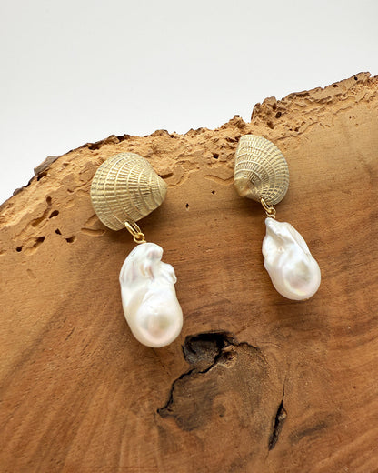 Pair of earrings with shell and baroque pearl design on a wooden surface