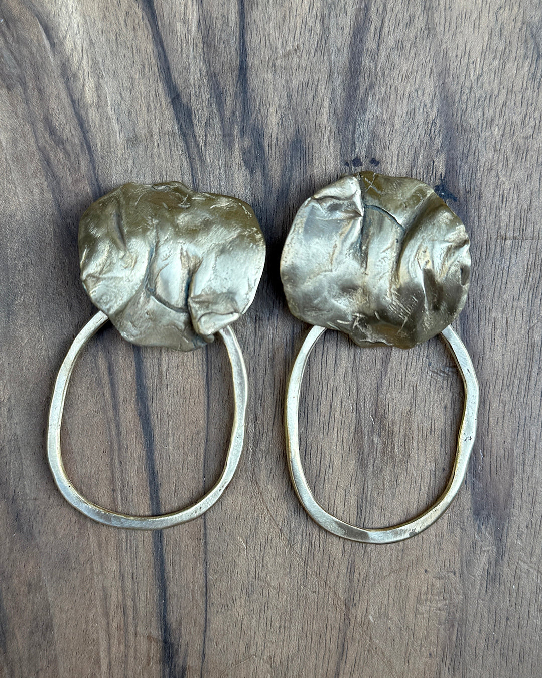 Pair of bronze hoop earrings with coral detail on a wooden surface