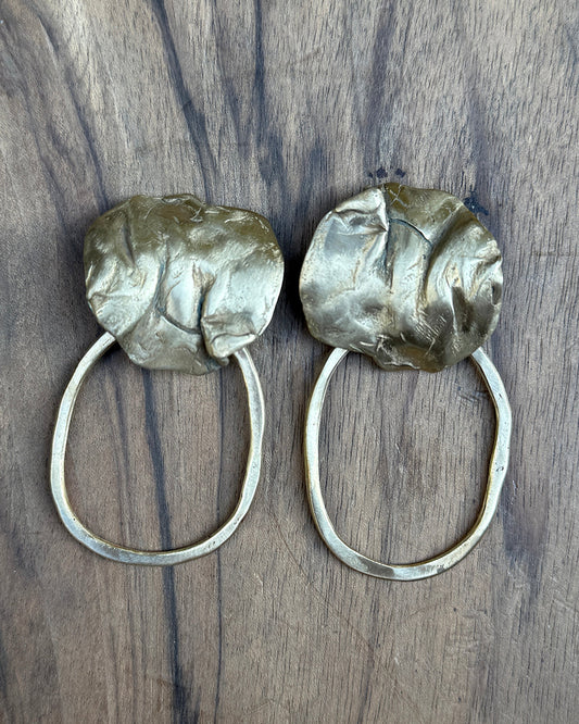 Pair of bronze hoop earrings with coral detail on a wooden surface