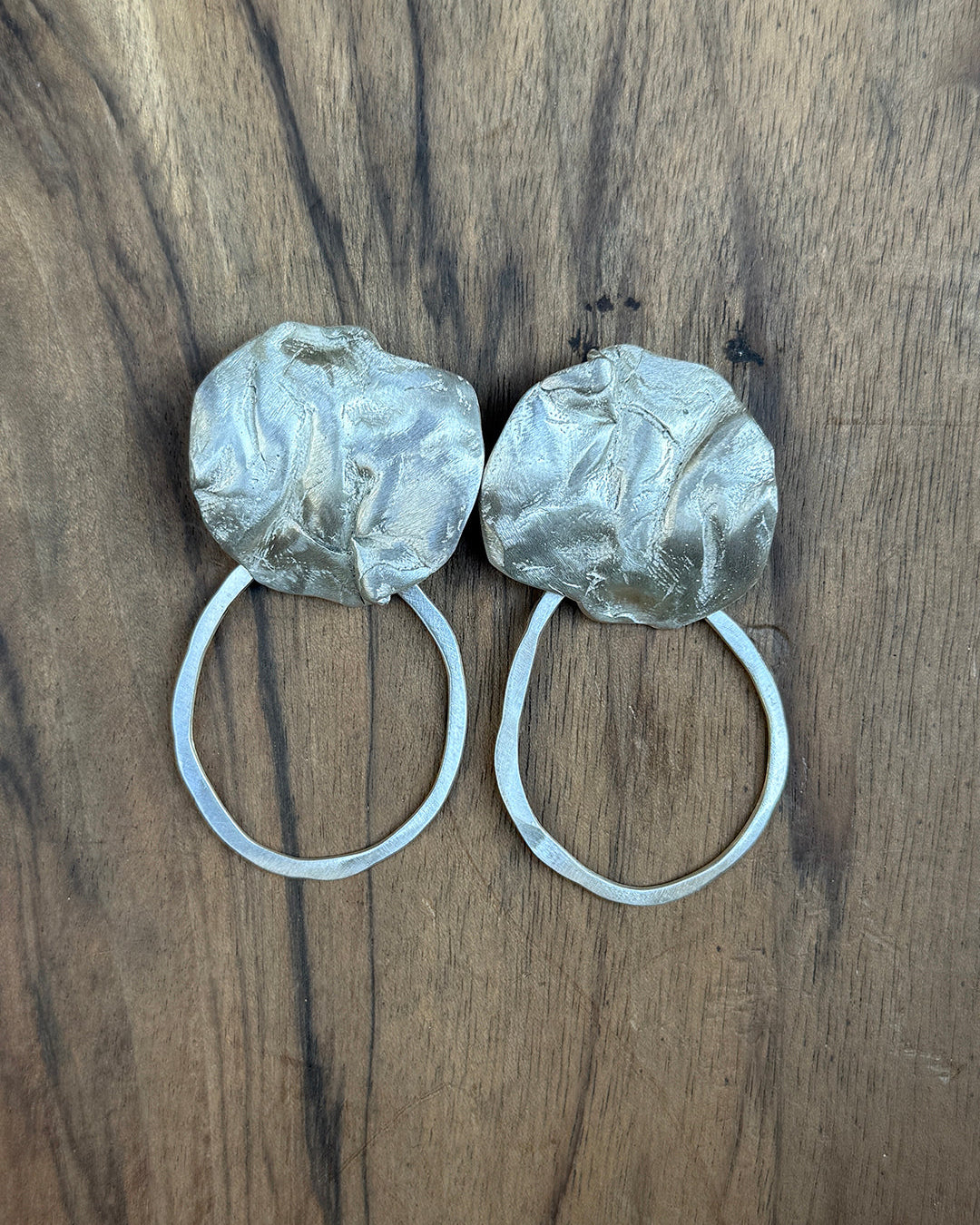 Two silver hoop earrings with coral detail on a wooden surface