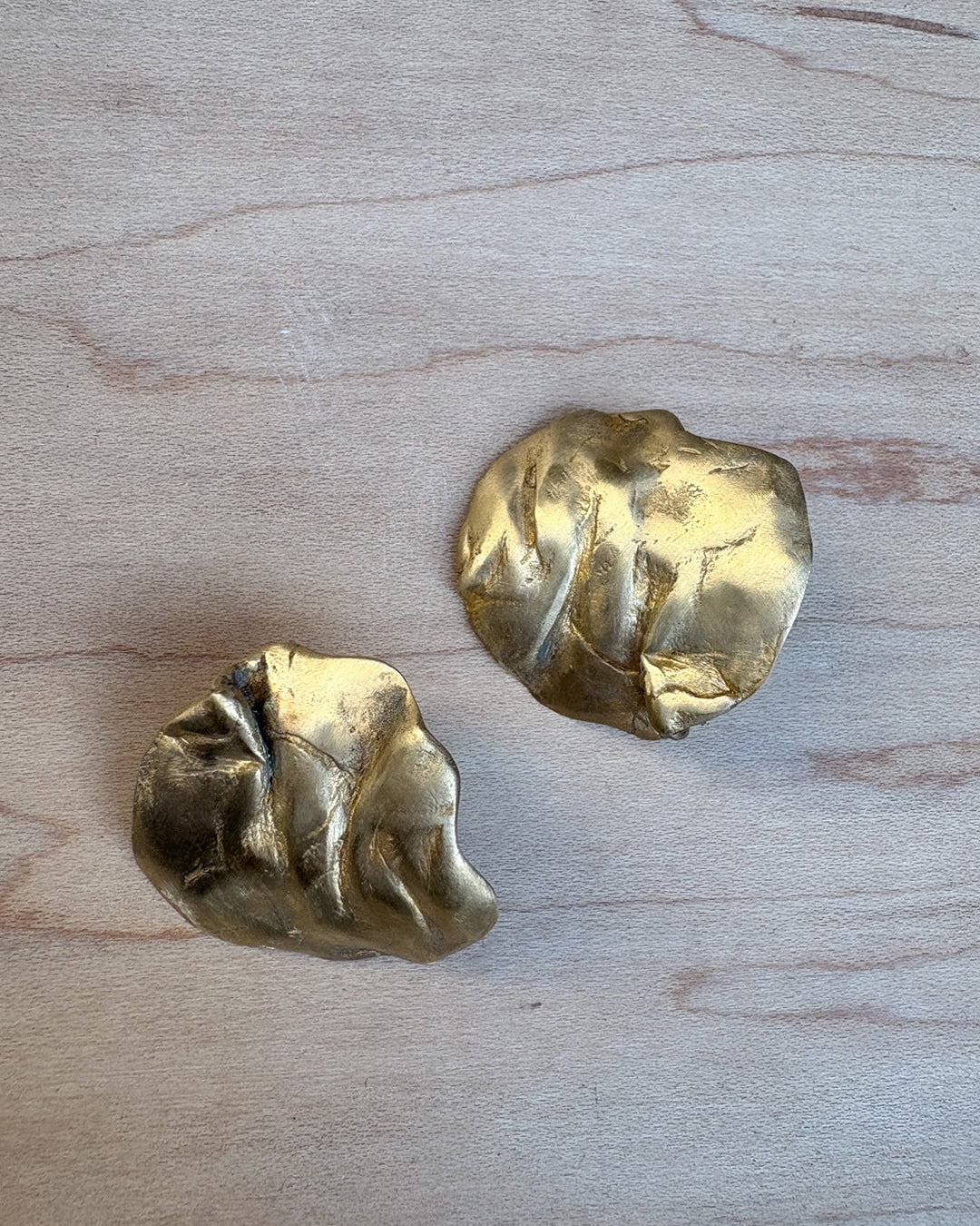 Two gold coral-shaped earrings on a light wood surface