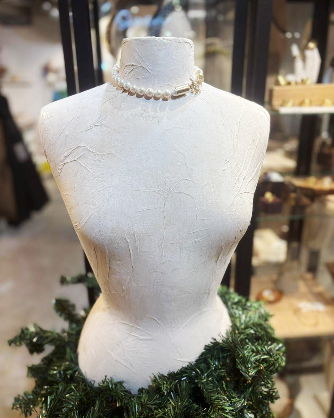 Mannequin torso wearing a skirt of green holiday foliage and a pearl choker necklace.