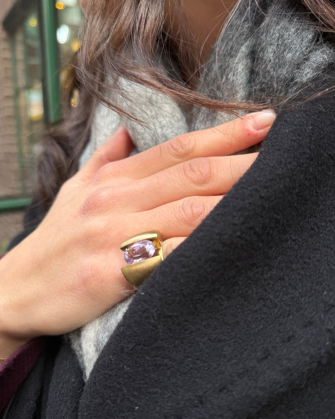 Close-up of a hand wearing a gold ring with a pink gemstone, blurred background