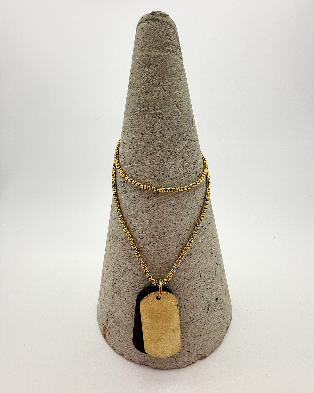 Gold necklace with a dog tag on a textured gray cone stand against a white background