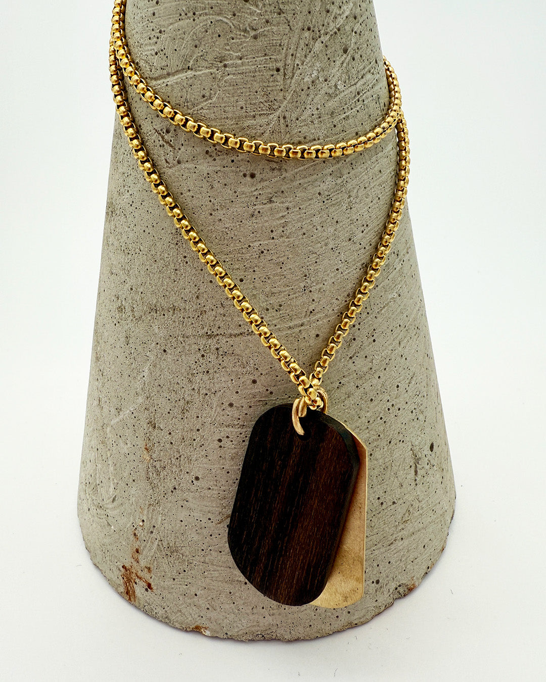 Gold necklace with a dark pendant on a textured gray stand.