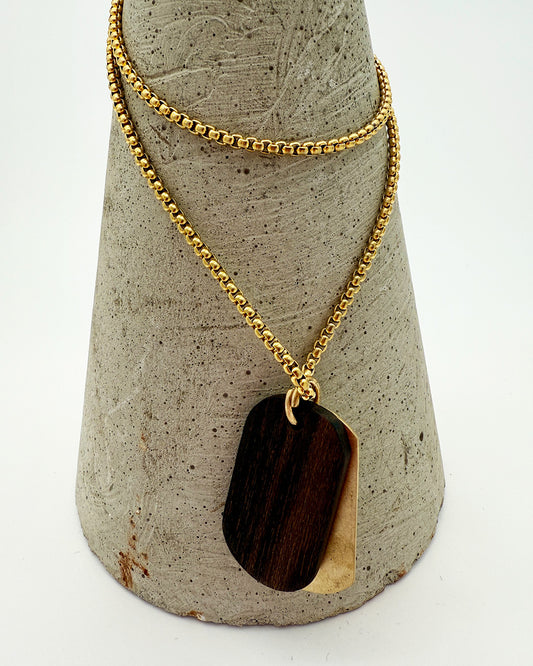 Gold necklace with a dark pendant on a textured gray stand.