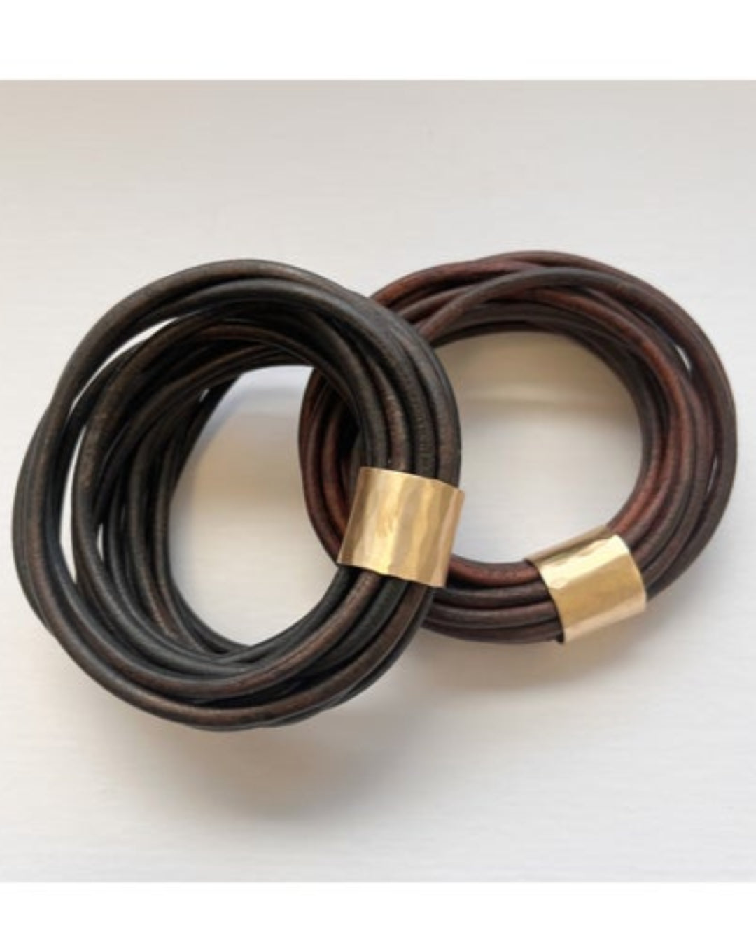 Two multistrand brown leather bracelets with gold details on a white background