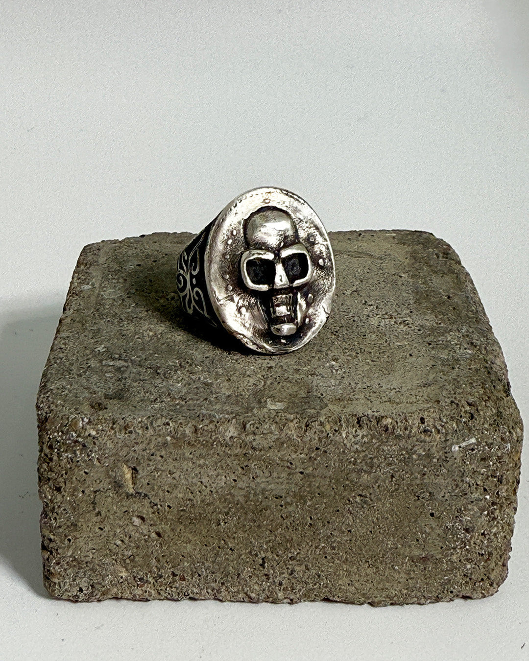 Silver skull ring on a concrete block with a plain background