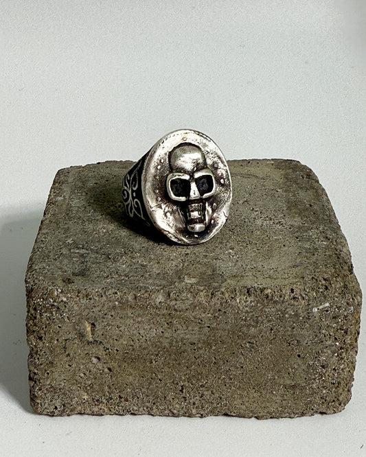Silver skull ring on a concrete block with a plain background