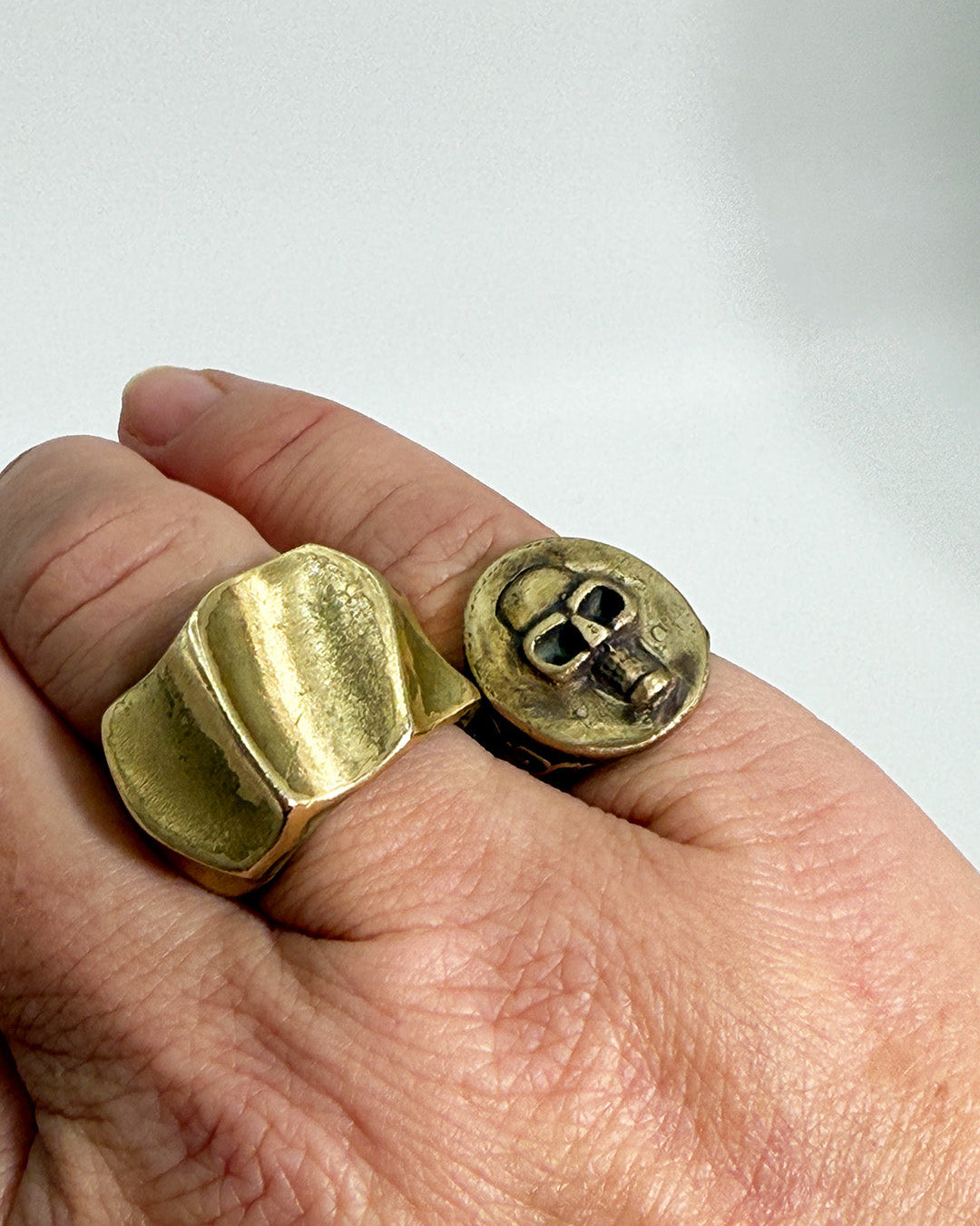 Gold ring with skull design on a finger against a white background