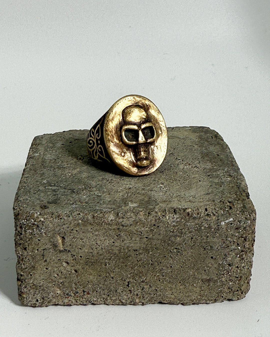 Gold ring with face design on a concrete block against a light gray background