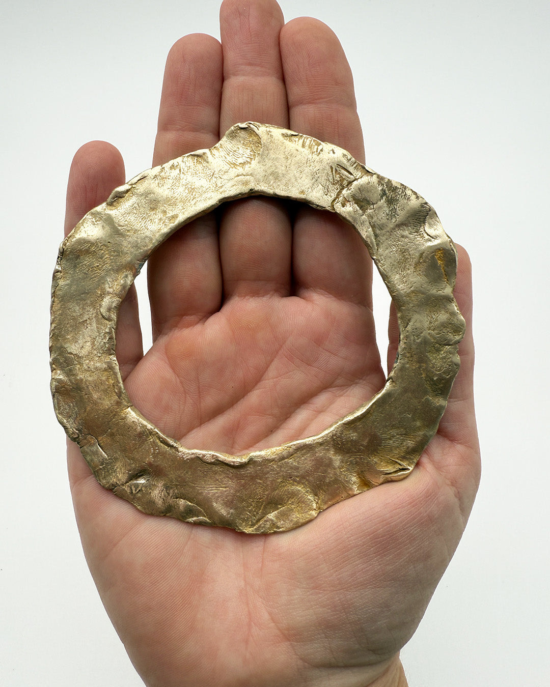 Hand holding a large gold ring against a white background