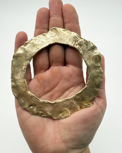 Hand holding a large gold ring against a white background