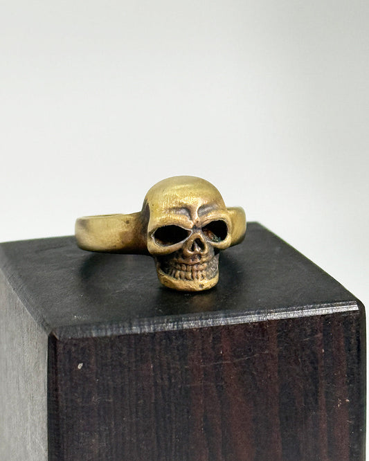 Brass skull ring on a wooden block with a white background