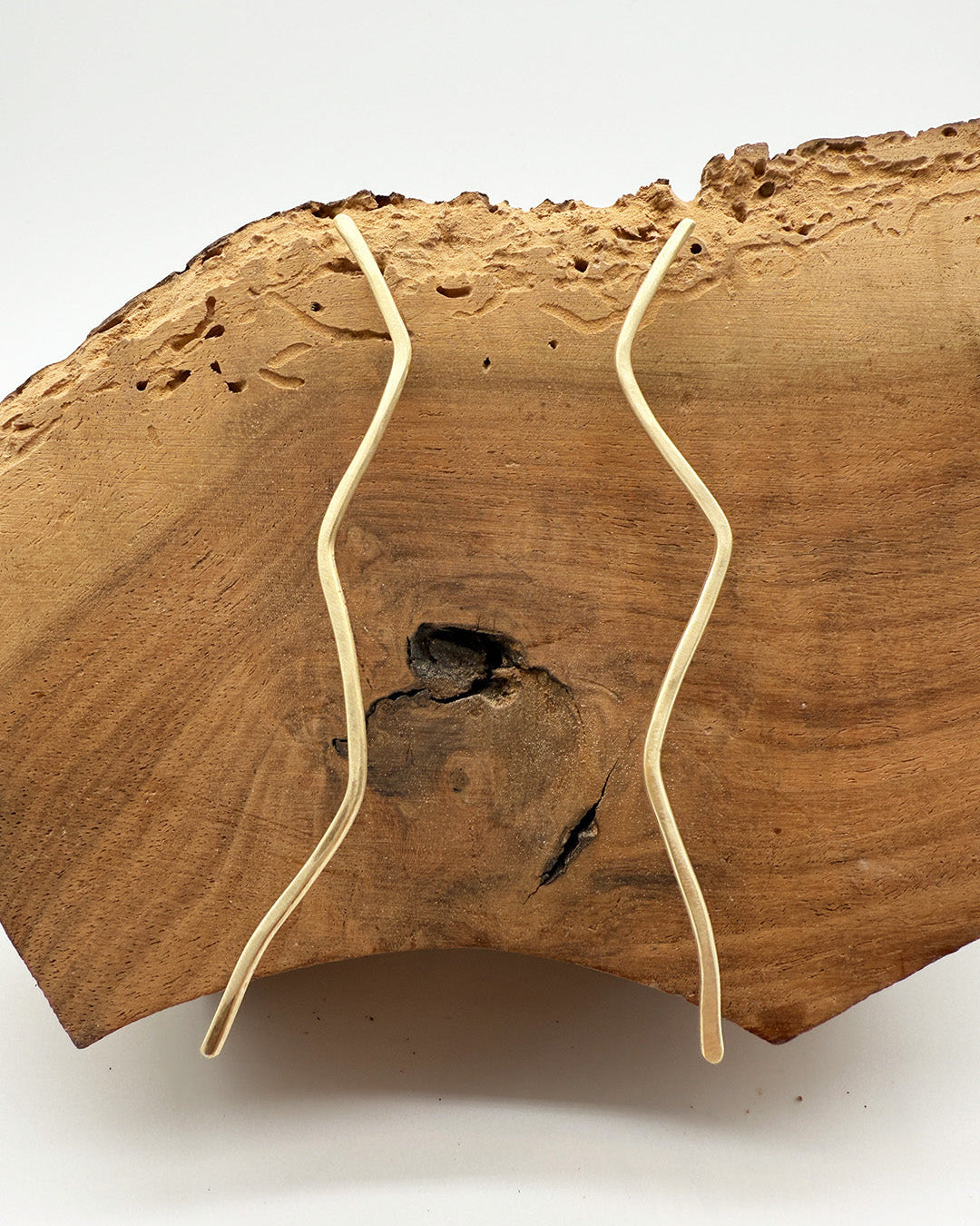 Two gold earrings on a wooden block with a white background